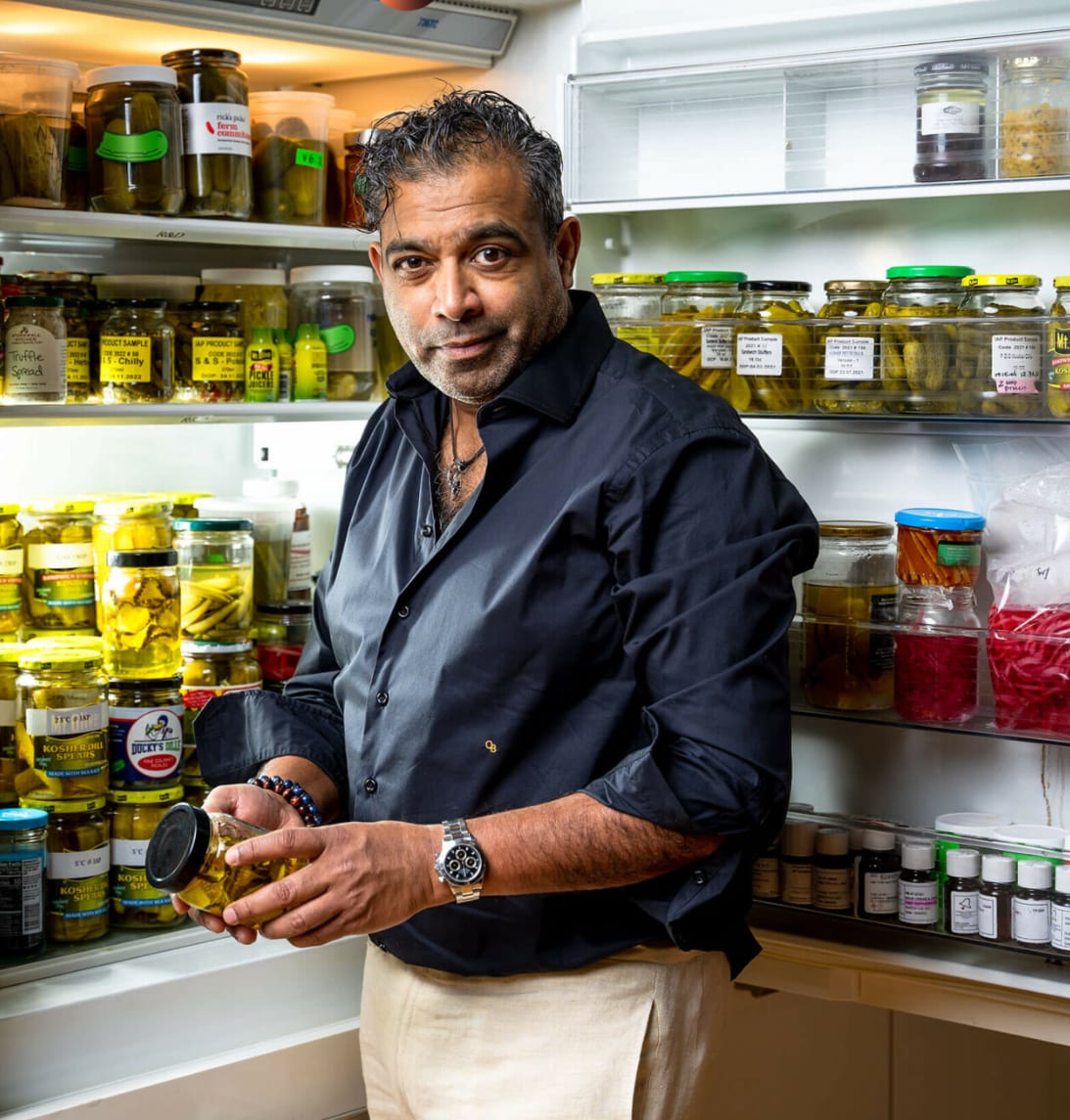 Murali Sundar holding a jar of pickles in front of Marcatus QED's refrigerated shelves of labelled product samples
