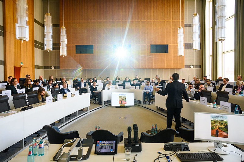 A speaker addressing delegates seated around the horseshoe table at the ESMT Berlin Sustainable Business Roundtable