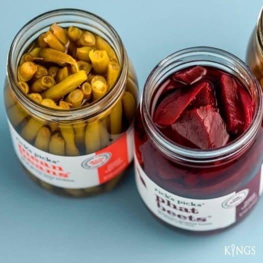 Retail jars of pickled beans and pickled beets on a pale blue background